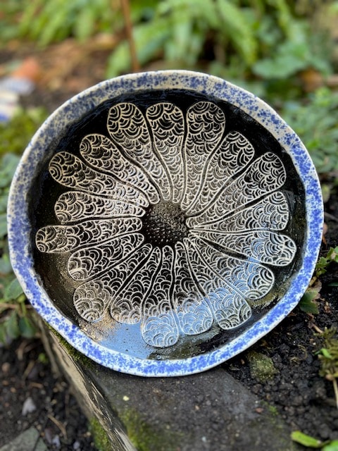 Handmade ceramic bowl with black and blue splatter glaze and intricate sgraffito daisy pattern